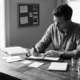 A man focused on writing in a planner at a minimalist wooden desk.